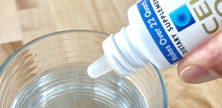 Person's Hand Pouring Cellfood into a Glass of Water